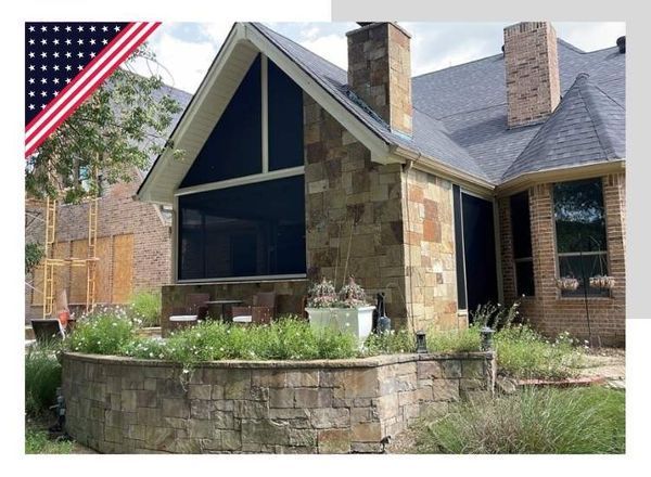 Stone house with screened porch, chimney, and garden. American flag in corner.
