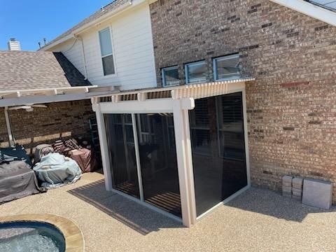 Screened porch attached to a brick house with a pergola-style roof. The porch is near a pool.