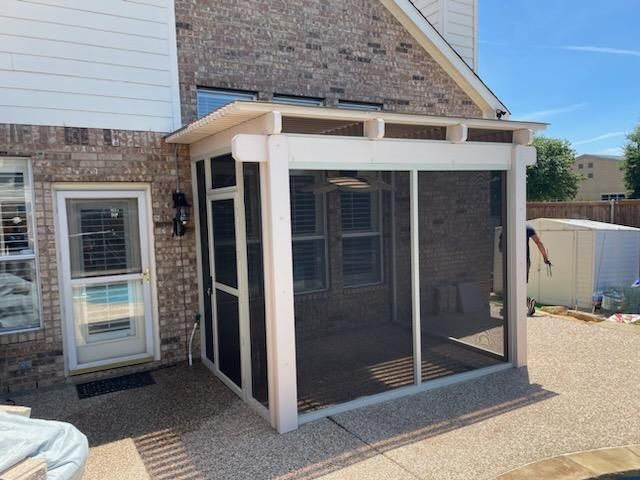 Screened-in porch attached to a brick house, featuring a white frame, screen walls, and a door, with a pool visible.