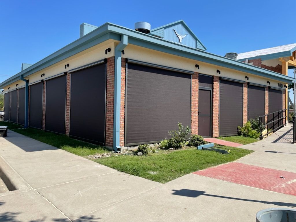 Building with brown roller shutters, brick accents, and blue roof under a clear sky.