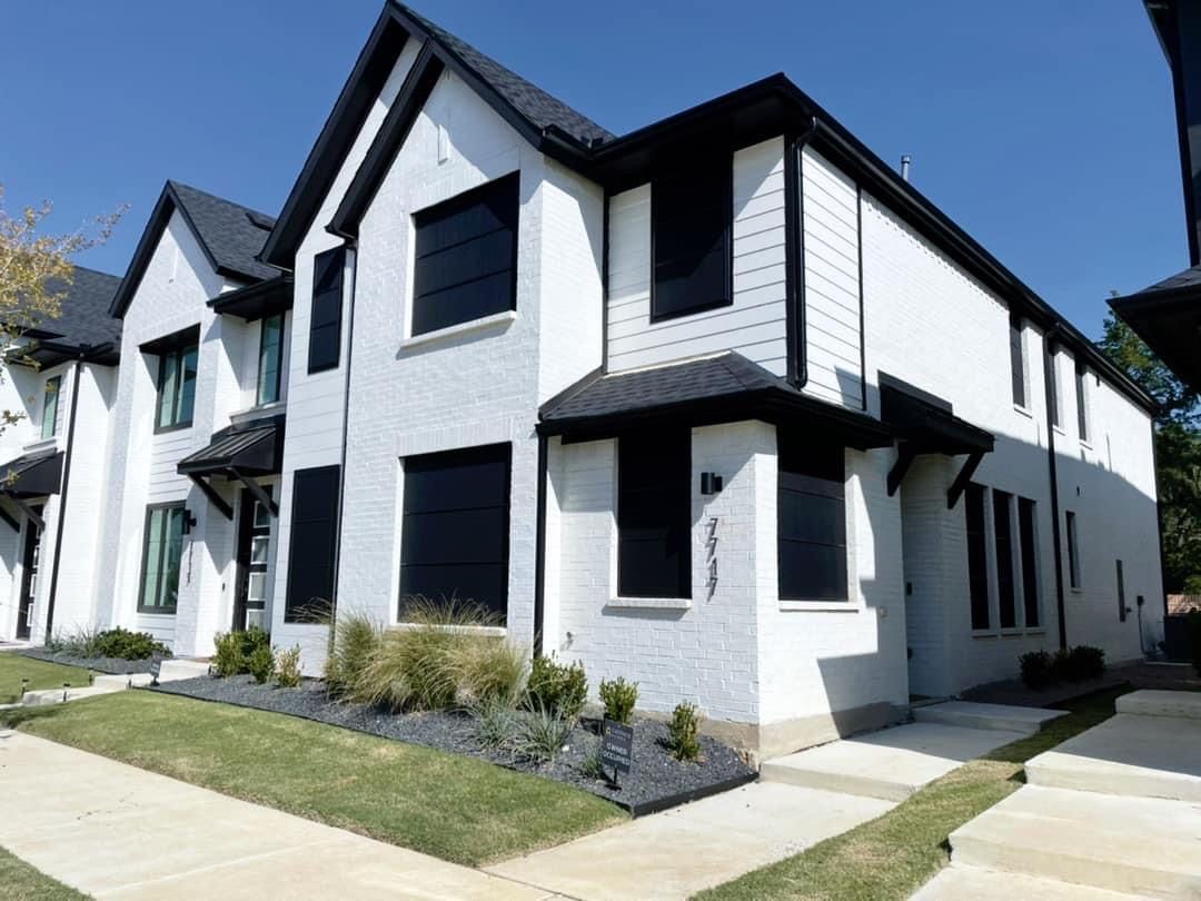 White two-story townhomes with black trim and windows, a manicured lawn, and a clear blue sky.