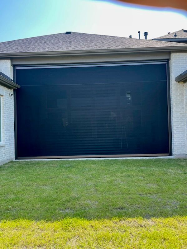 Large black retractable screen installed on a brick home’s patio.