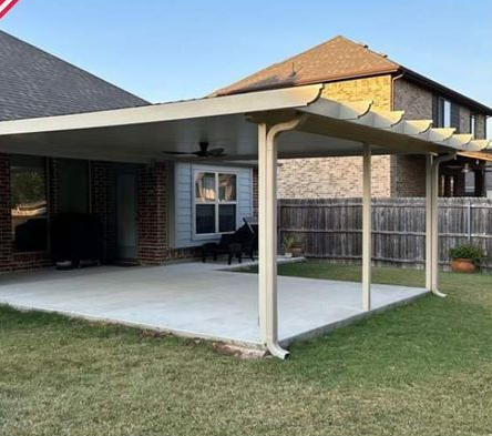 Covered backyard patio with white posts and ceiling fan beside a brick house and fenced lawn
