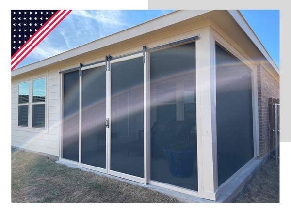 Exterior view of a screened-in porch with sliding glass doors, white trim, and a brick wall. American flag in the corner.