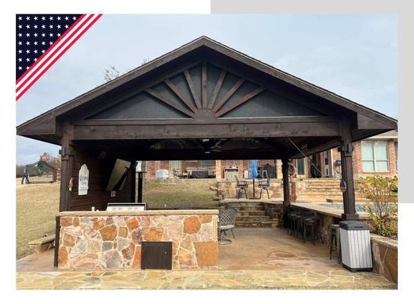 Outdoor patio with a brown wooden pergola, stone countertop, fireplace, and the American flag.