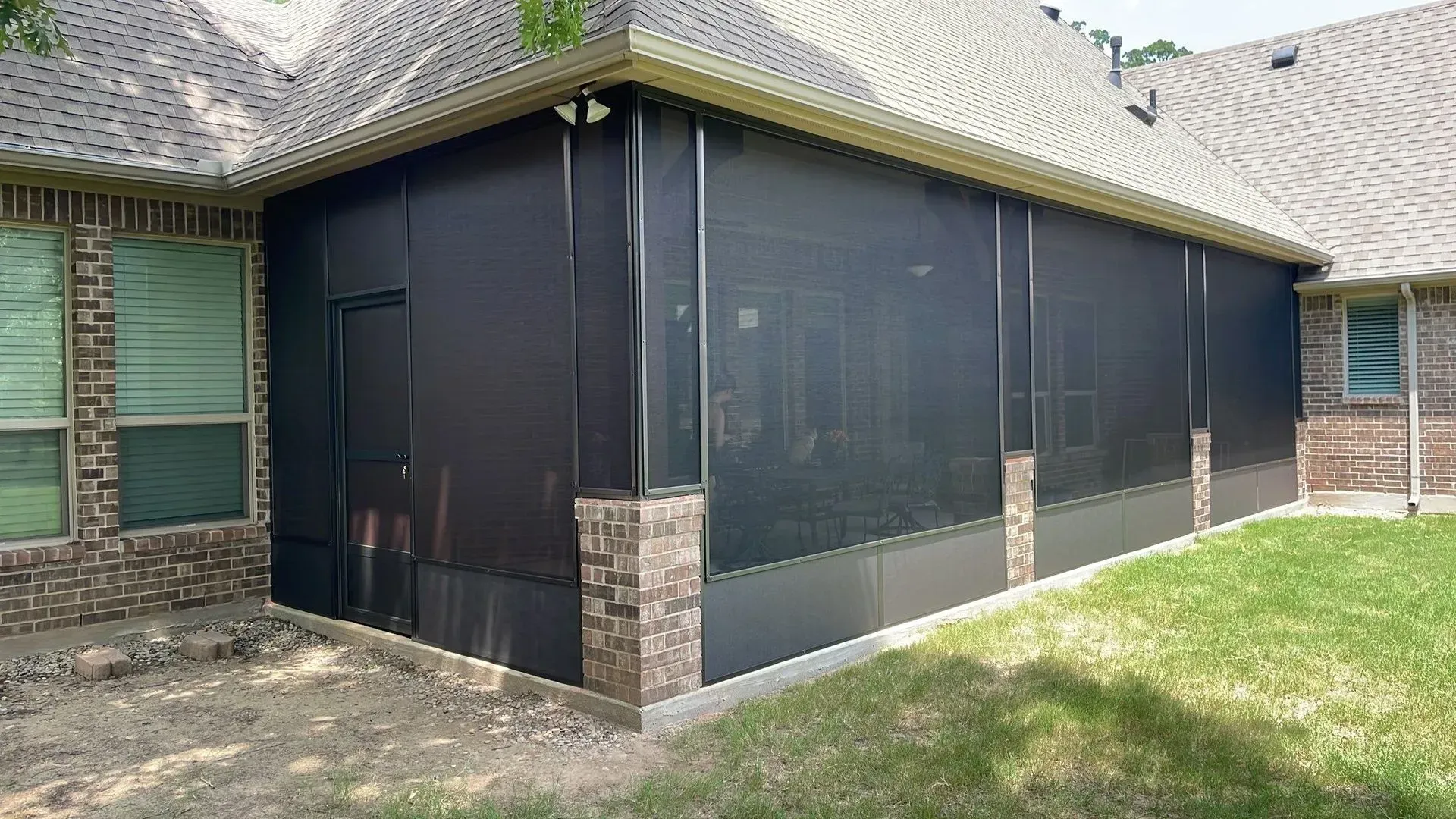 Brick house patio enclosed with black mesh screens and a screened roof over a grassy yard