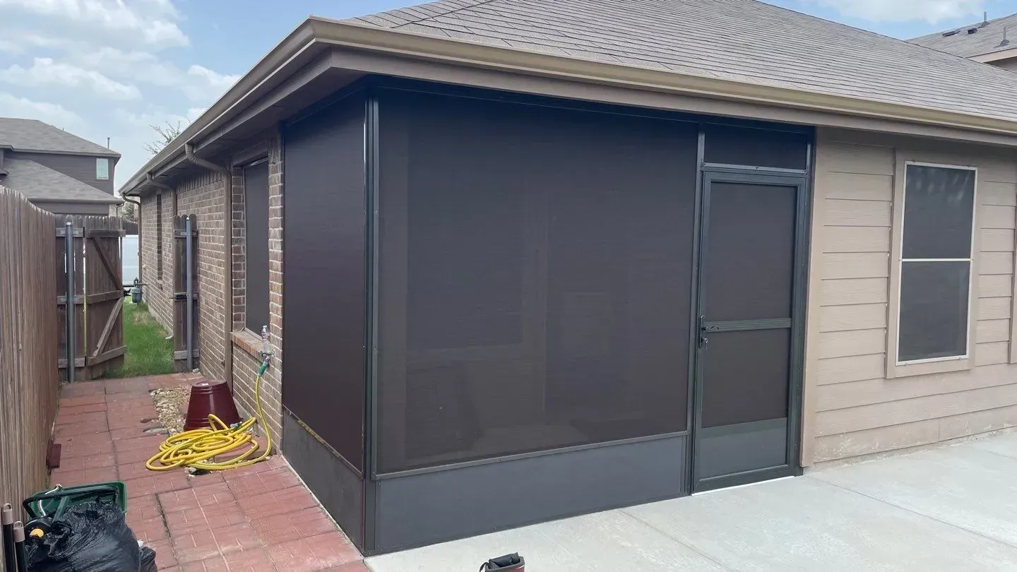 Screened patio beside a beige house with a brick walkway and screened door.