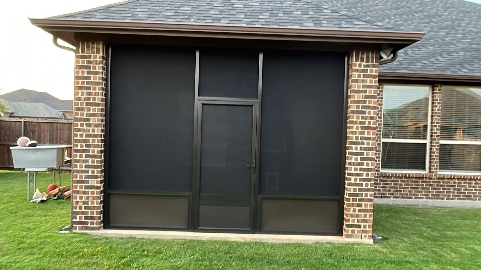 Black screened patio or shed with brick sides and shingled roof in a grassy backyard