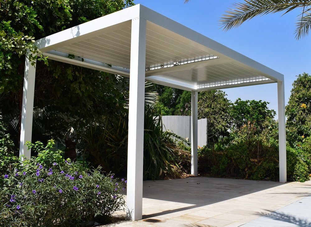 White modern pergola in a garden, with a partially shaded roof.