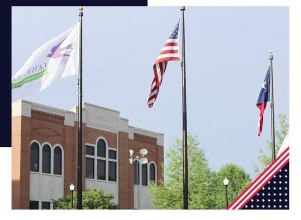 Flags on poles in front of a brick building. The American flag and Texas flag are visible.