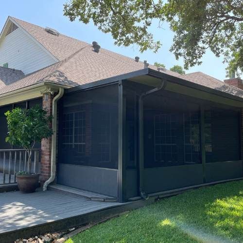 Screened-in porch on a house with a brick exterior, grey screens, and a small tree in a pot.