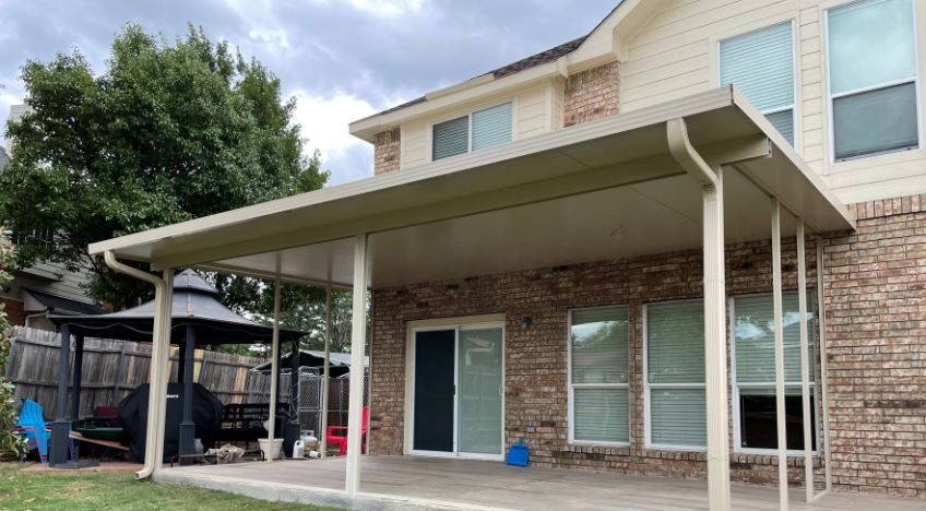 Backyard patio with a large covered pergola beside a brick house, and a sliding glass door underneath.