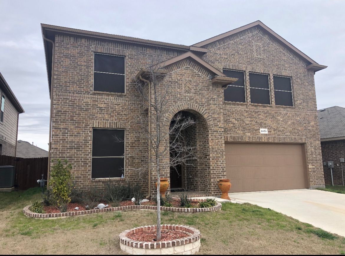 Two-story brick house with arched entrance and tan garage door. Lawn in front.