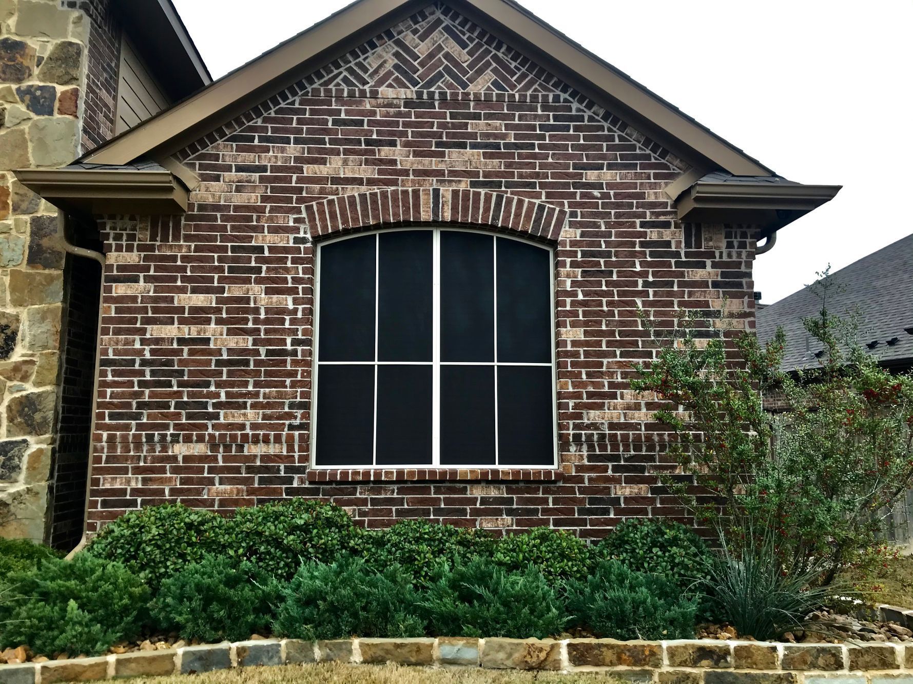 Brick home exterior with arched window, dark screen, and landscaping.