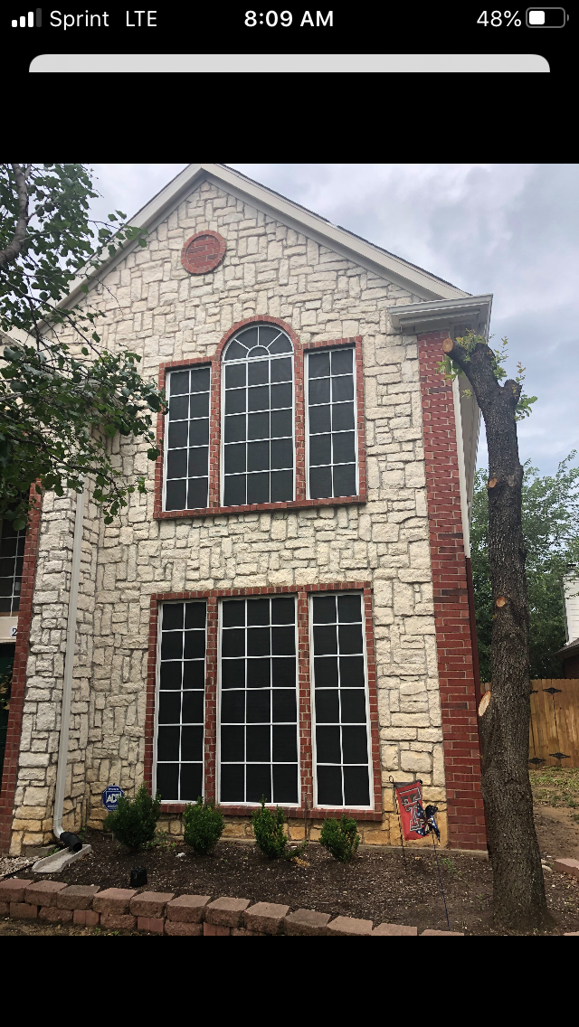 Two-story house with stone facade, brick trim, and large windows.  Small front yard with shrubbery.