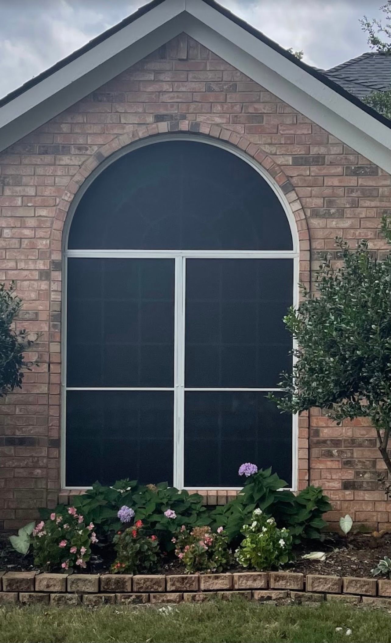 Large arched window with a black screen, brick facade, and small garden below.