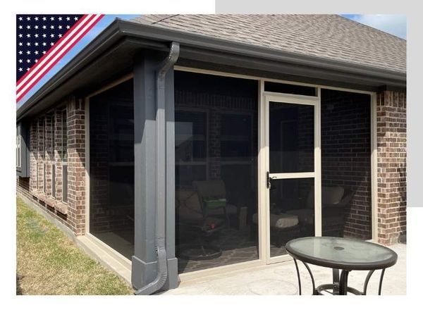 Screened-in porch attached to a brick house. Gray trim and door frame with black screening. A table sits outside the door.