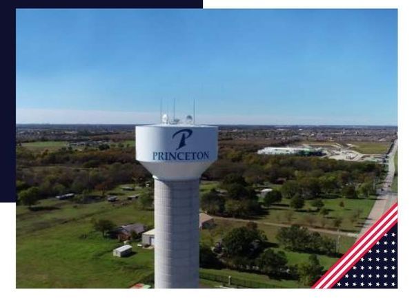 Princeton, TX water tower with logo, set against a green field and a clear blue sky.