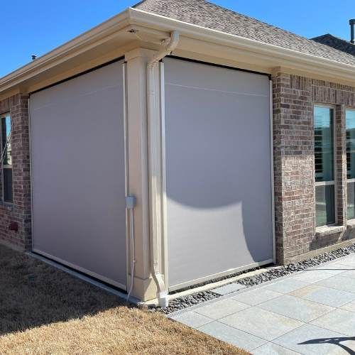 Light gray outdoor shade installed on a brick patio corner of a house.