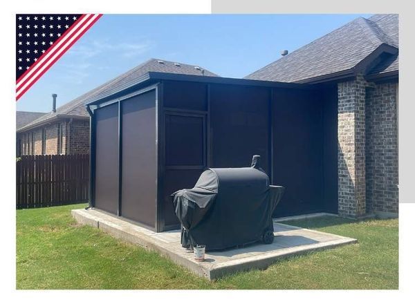 A brown screened outdoor enclosure with a covered grill on a concrete pad. An American flag is in the upper left corner.