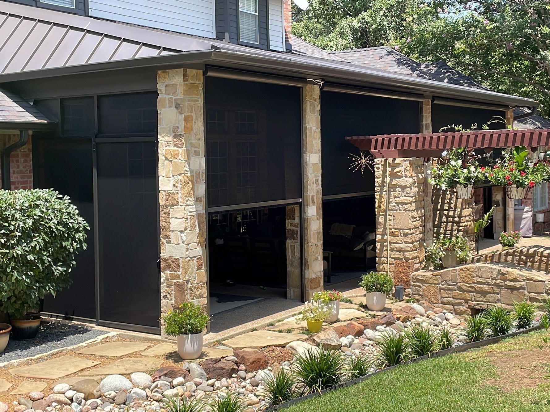 Home exterior with retractable black screens, stone columns, and landscaped yard.
