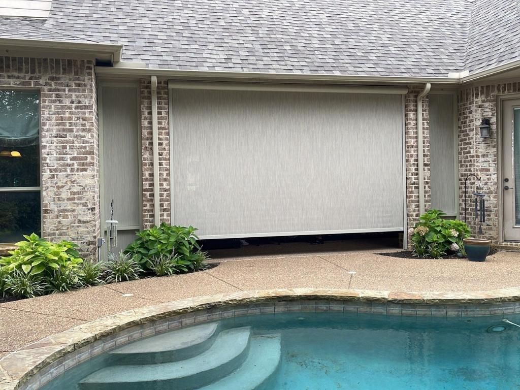 Outdoor patio with lowered beige sun screen, brick building, and pool.