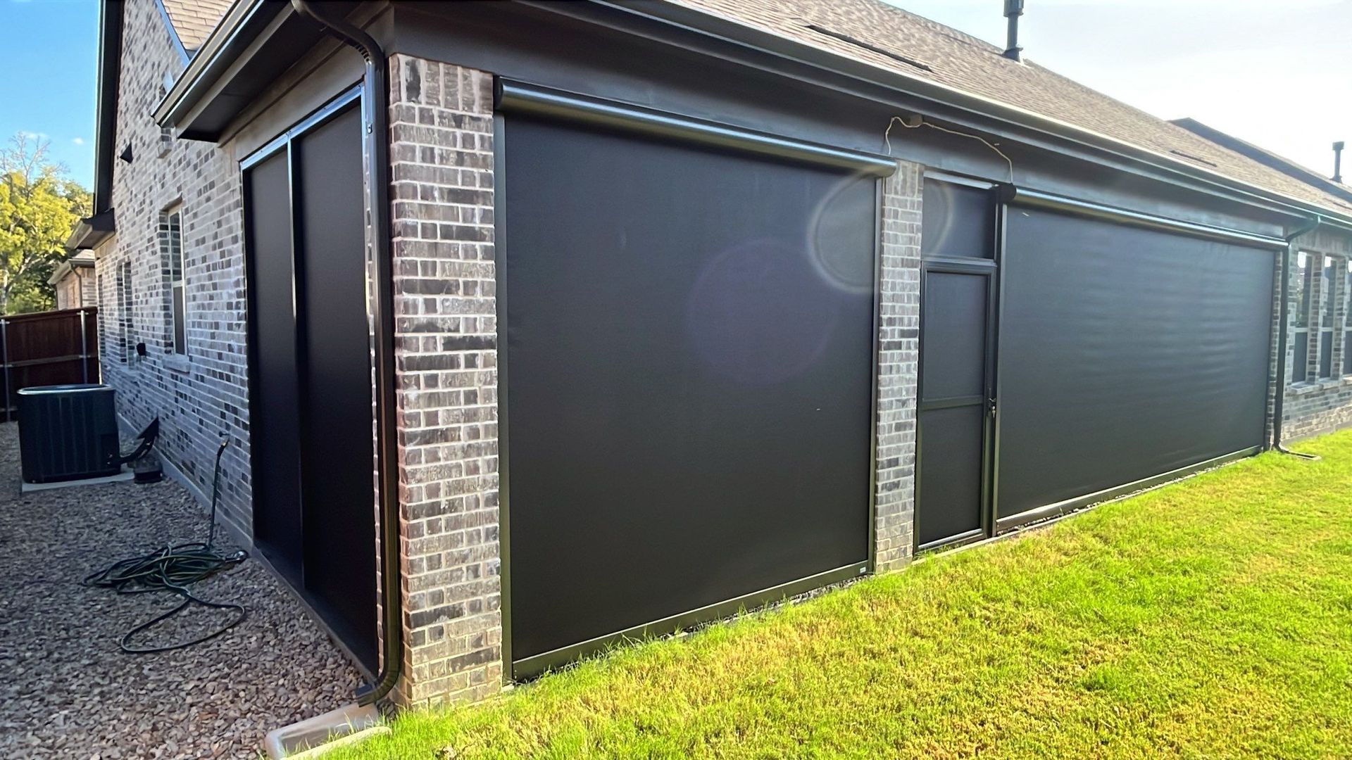 Black outdoor sun shades installed on a brick building with green grass and sky visible.