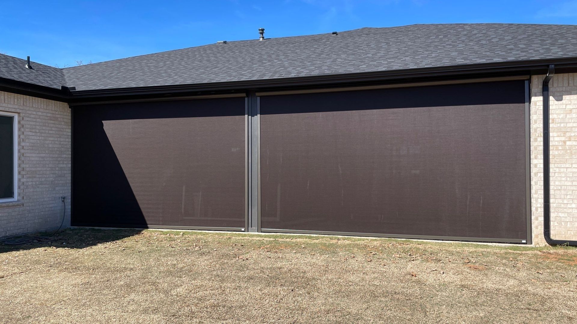 Brown outdoor sun shades on a brick building, casting shadows onto the grass.