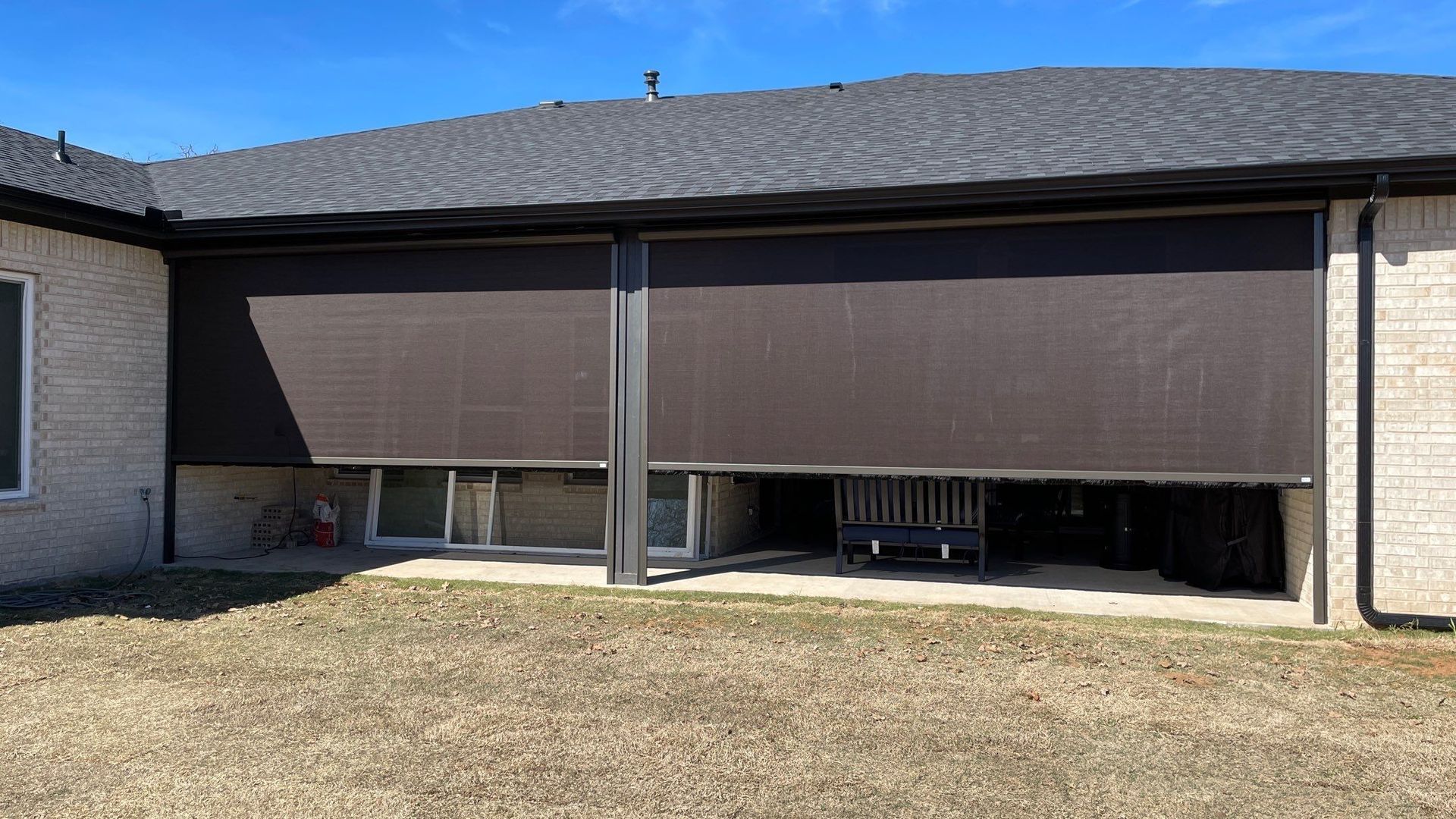 Two large, dark brown outdoor sun shades partially cover the patio. Gray brick house, brown grass.