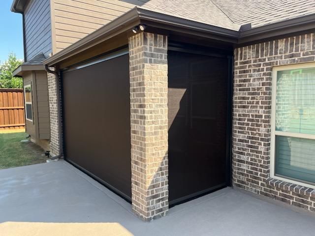 Black outdoor shade covers a brick patio enclosure. Brown roof and brick exterior visible.