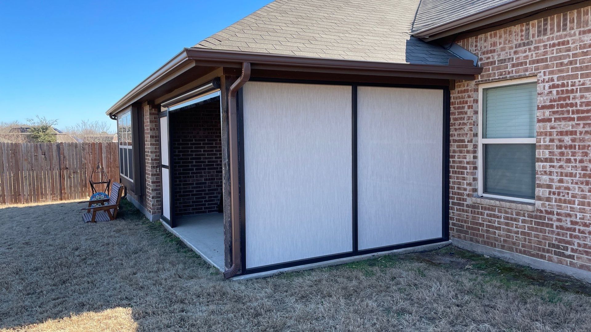 Covered patio with retractable screens, next to a brick house on a sunny day.