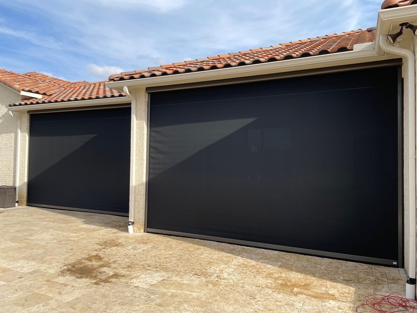 Black retractable sun shades covering garage doors under a red tile roof.