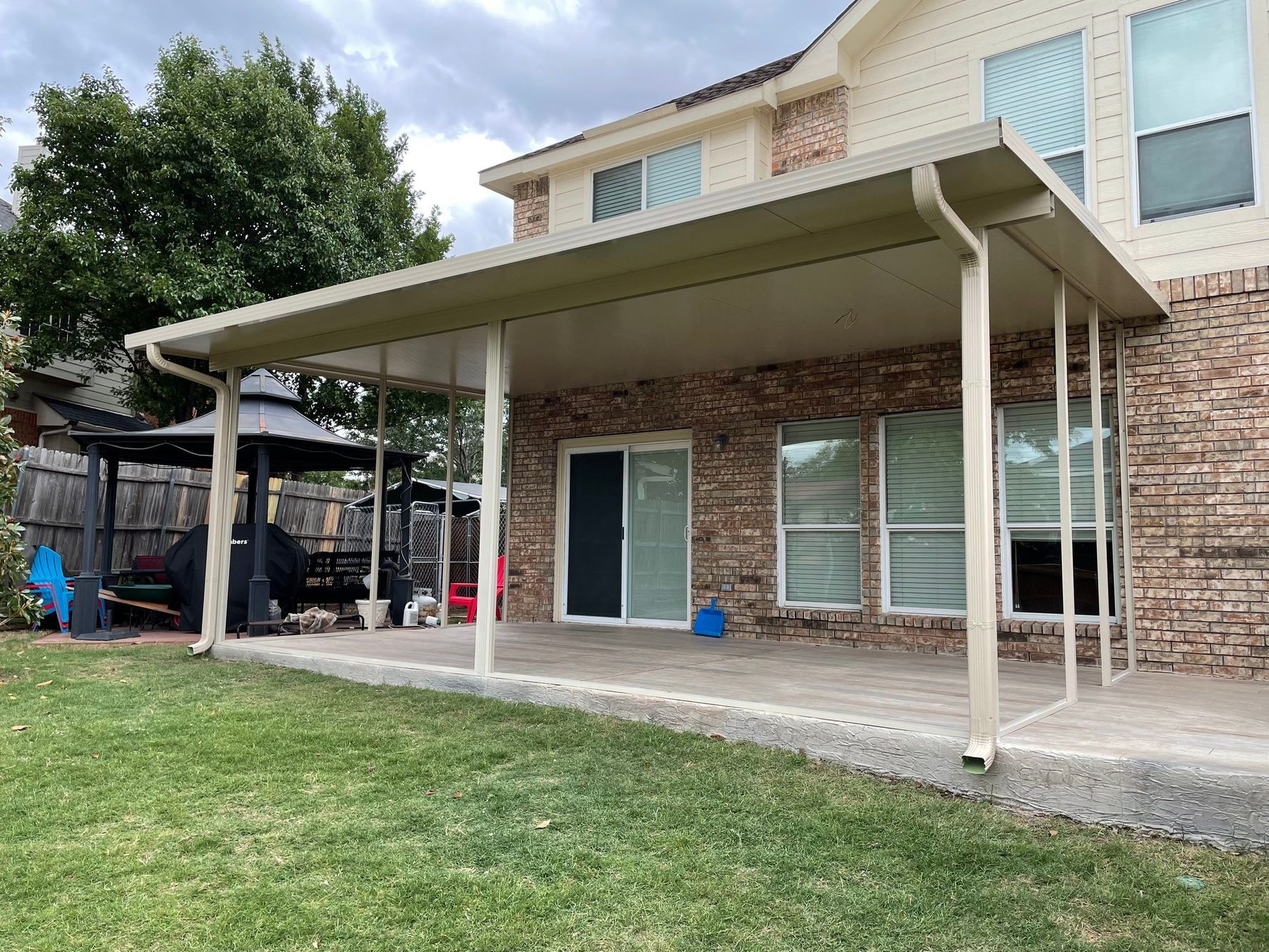 Backyard patio with a covered seating area. Brick house, concrete patio, green grass, and a gazebo.