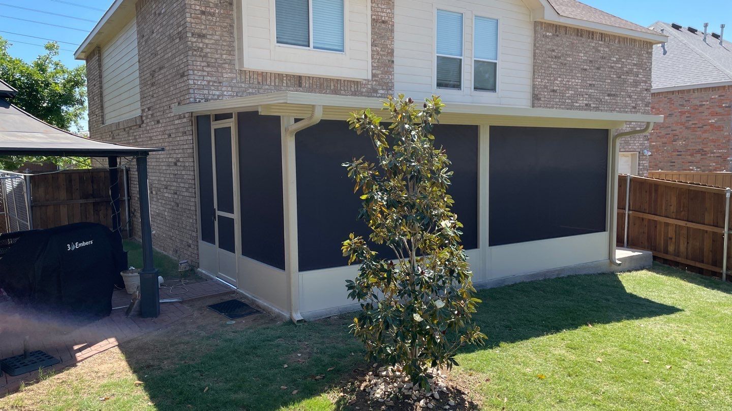 Screened-in porch attached to a brick house with a small tree in the yard.