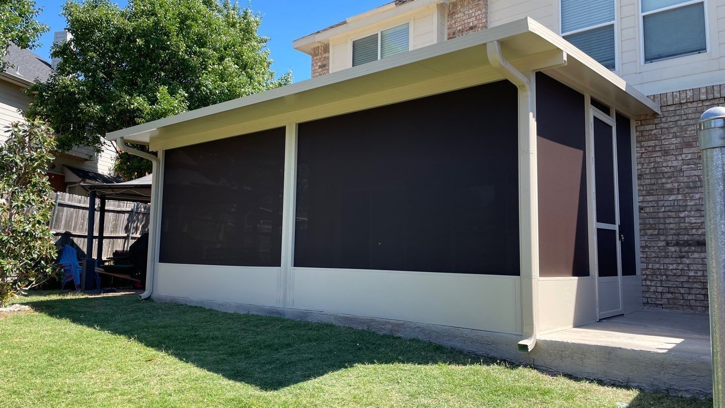 Screened-in porch attached to a brick house with a green lawn. Dark screens provide shade.
