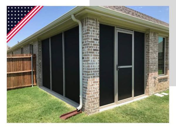 Screened-in patio enclosure with black mesh panels and door against brick wall.