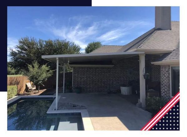A patio with a pool in the foreground. A white canopy extends from a brick house. Blue sky overhead.