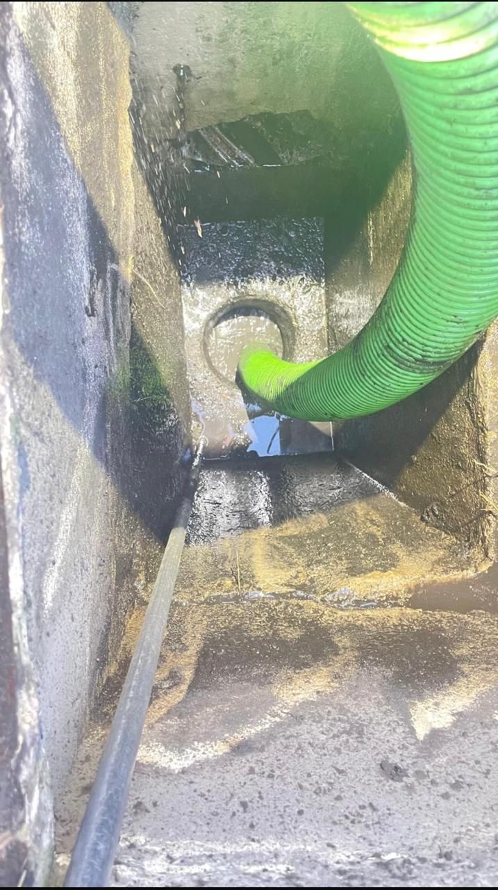 Green hose inside a dirty utility box, spraying water onto the bottom.