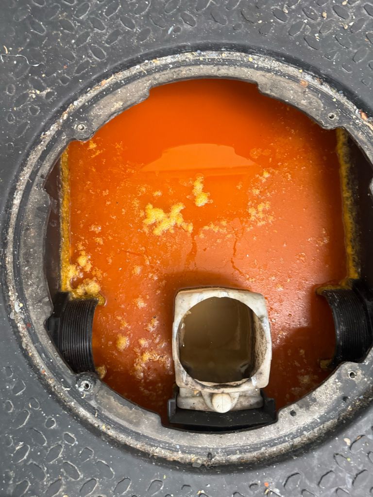 Close-up of a gray circular housing with orange residue and a small metal fitting at the bottom