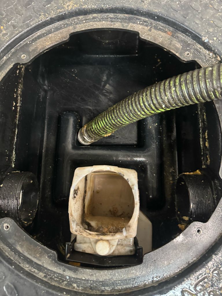 Close-up of a circular metal opening with a beige hose connector and a green corrugated hose inside.