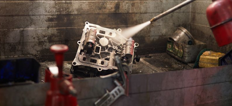 A metal engine component is being cleaned with a high-pressure spray, coating it in a red cleaning liquid. — JNL Crankshaft Services in Palmerston City, NT