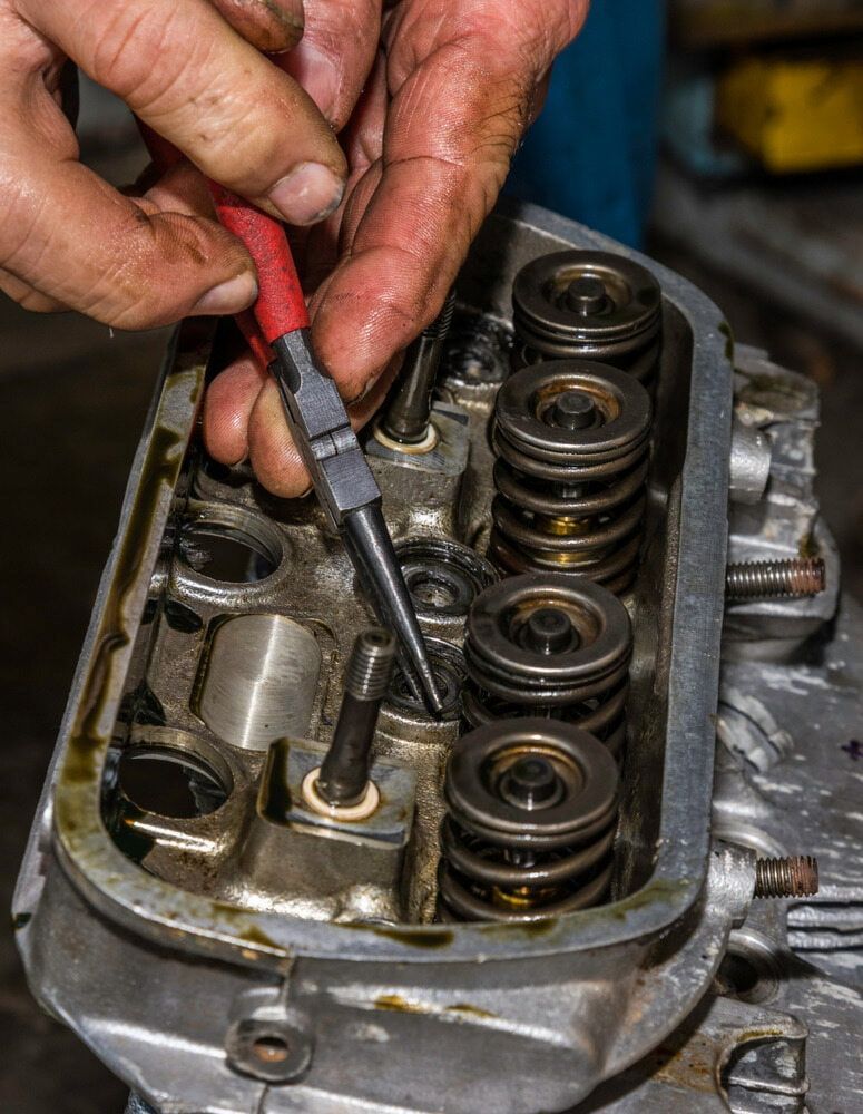 Hands Holding Needle-nose Pliers Near a Mechanical Engine Cylinder Head — JNL Crankshaft Services in Palmerston City, NT