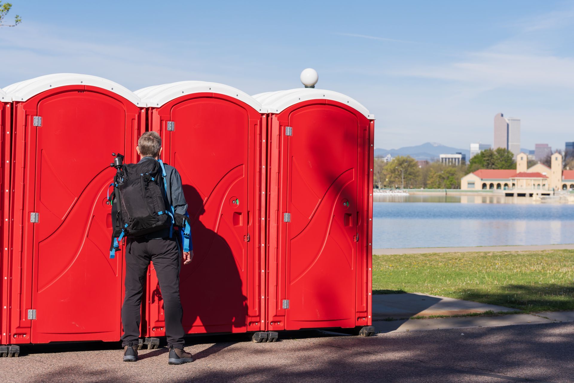 A man standing in front of a row of red portable toilet rental units, set up and ready for use. A man standing in front of a row of red portable toilet rental units, set up and ready for use.