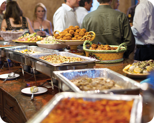 Buffet table with various dishes; people in background.