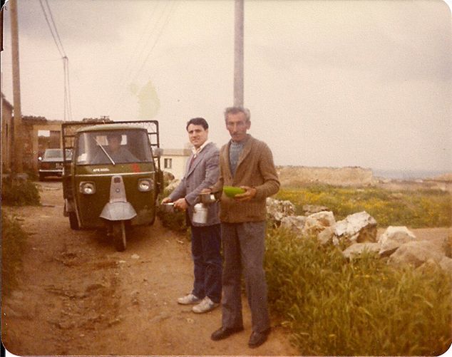 Two men stand near a green three-wheeled vehicle. 