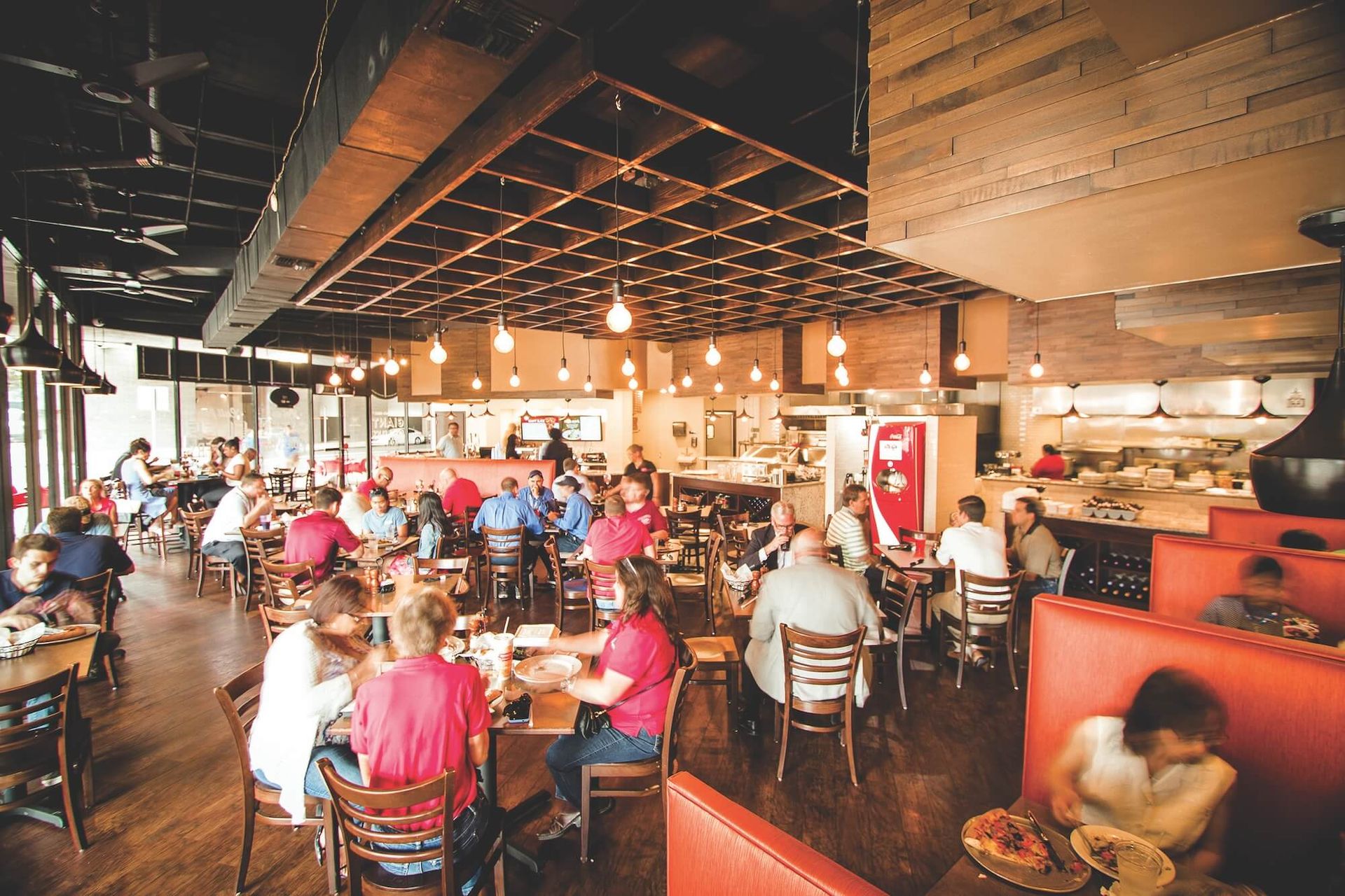 Busy restaurant dining room with many people seated at tables under warm hanging lights