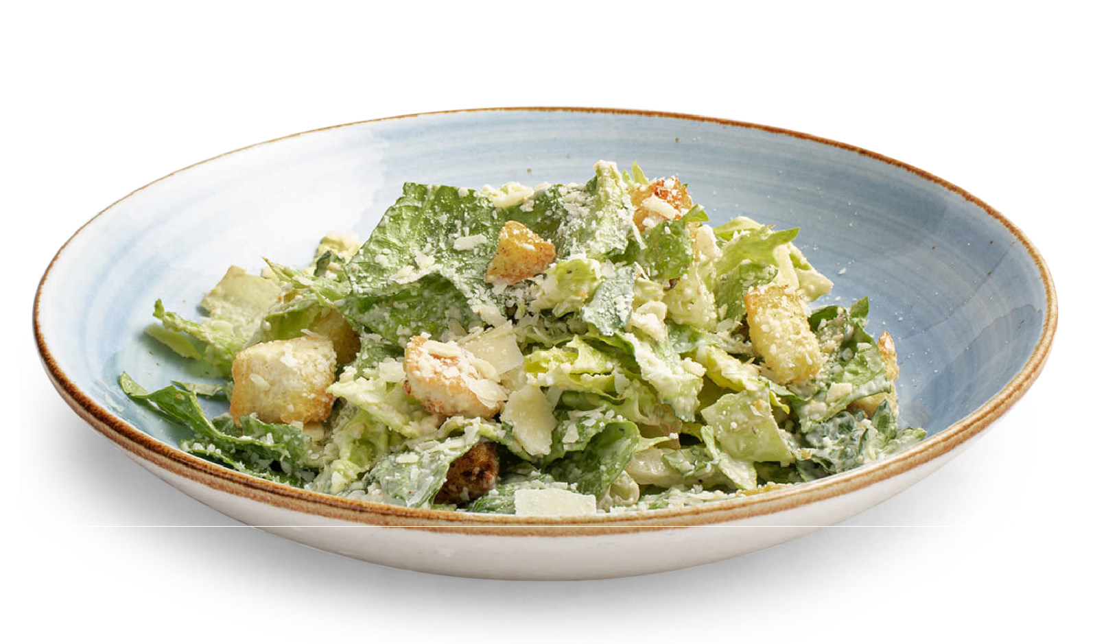 A Caesar salad with croutons and shaved cheese in a wide, shallow, light blue-rimmed ceramic bowl.