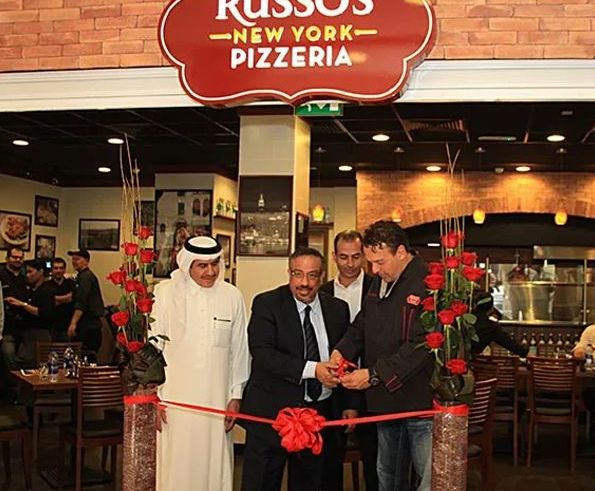 People cutting a ribbon to celebrate the opening of Russo's New York Pizzeria. The setting appears to be inside the restaurant.