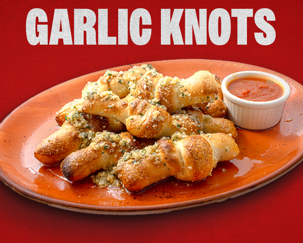 Garlic knots on an orange plate, served with marinara sauce; red background.