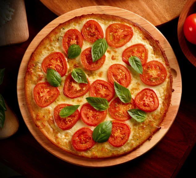 Pizza topped with sliced tomatoes and basil leaves on a wooden board.